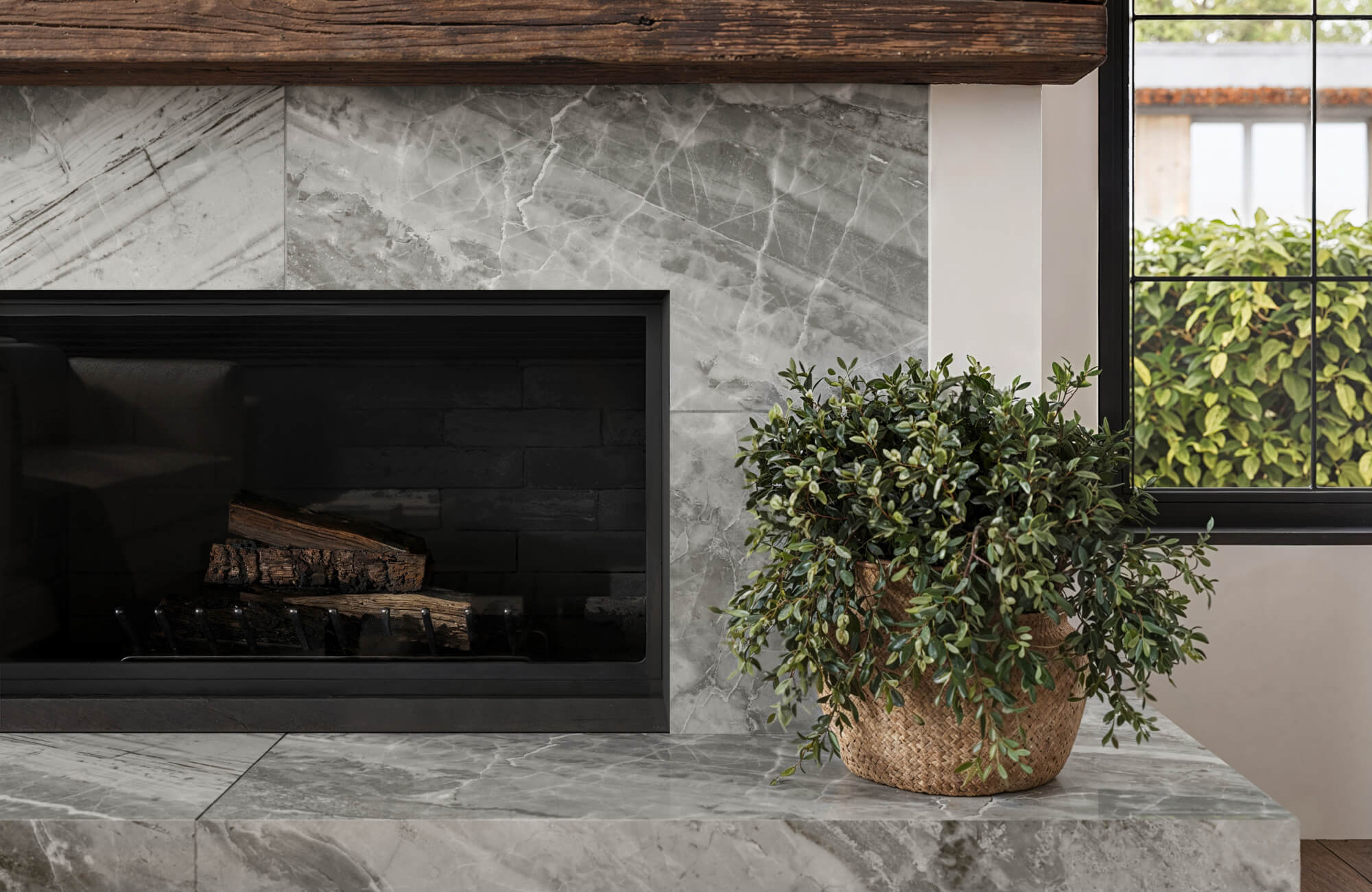 Cozy living room with a fireplace surrounded by Oniciata gray marble-look tiles, a rustic wooden mantle, and a potted plant adding a touch of greenery