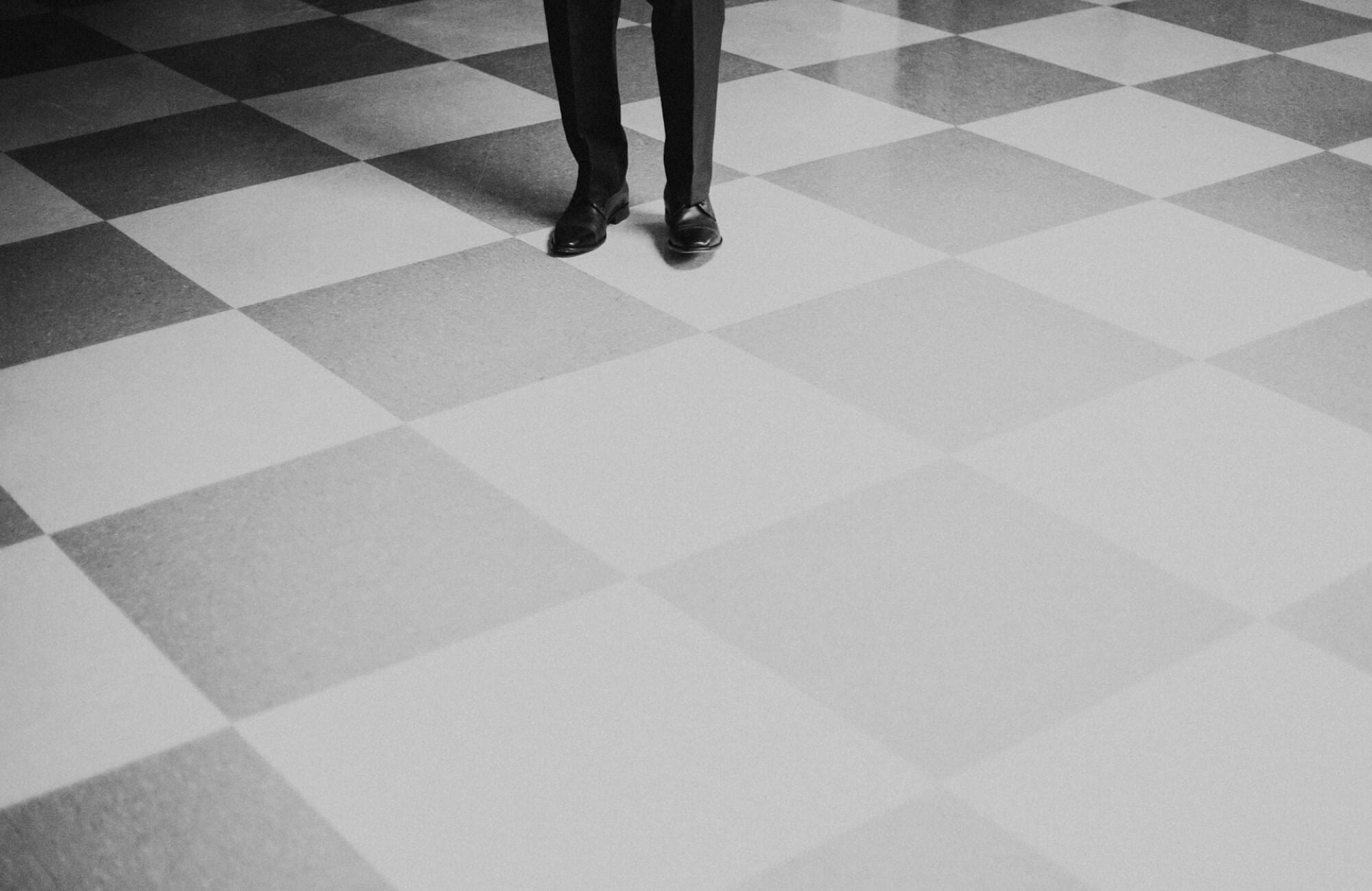 Monochrome checkerboard floor with white and black tiles, with a person in black dress shoes stepping into view