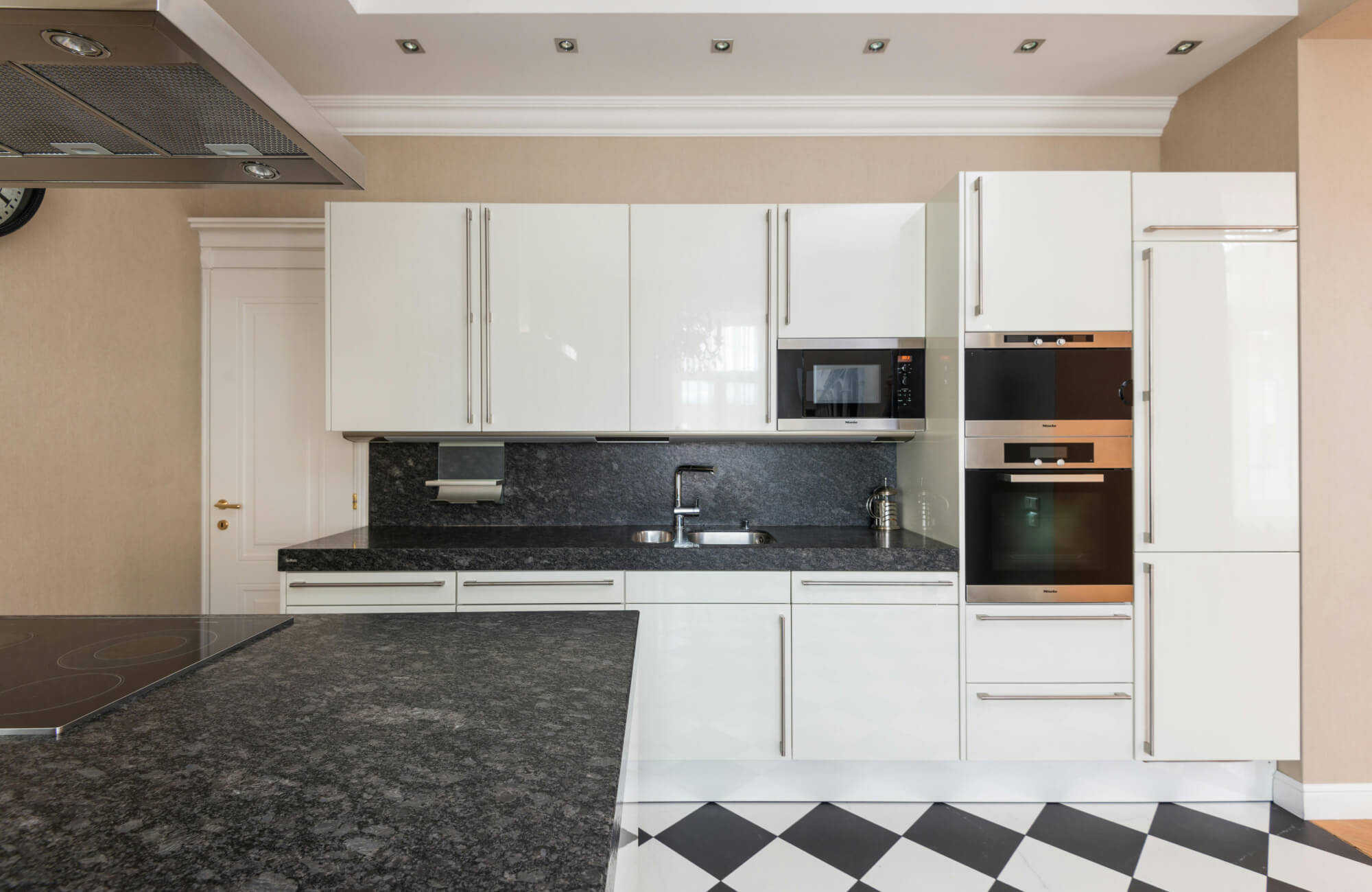 Modern kitchen featuring sleek white cabinetry with black countertops and a striking black and white checkerboard tile floor for bold contrast.