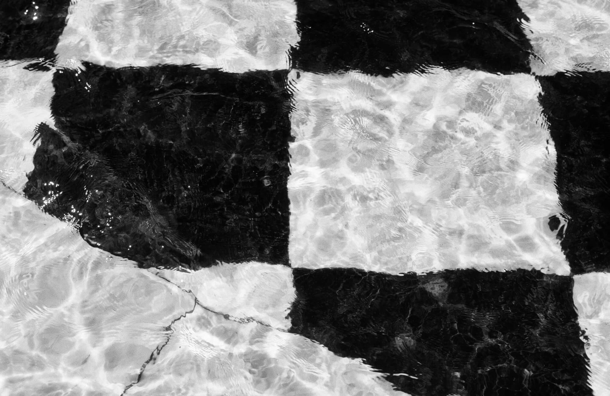 Black and white checkered tiles submerged under water, with light reflections creating a rippling effect.