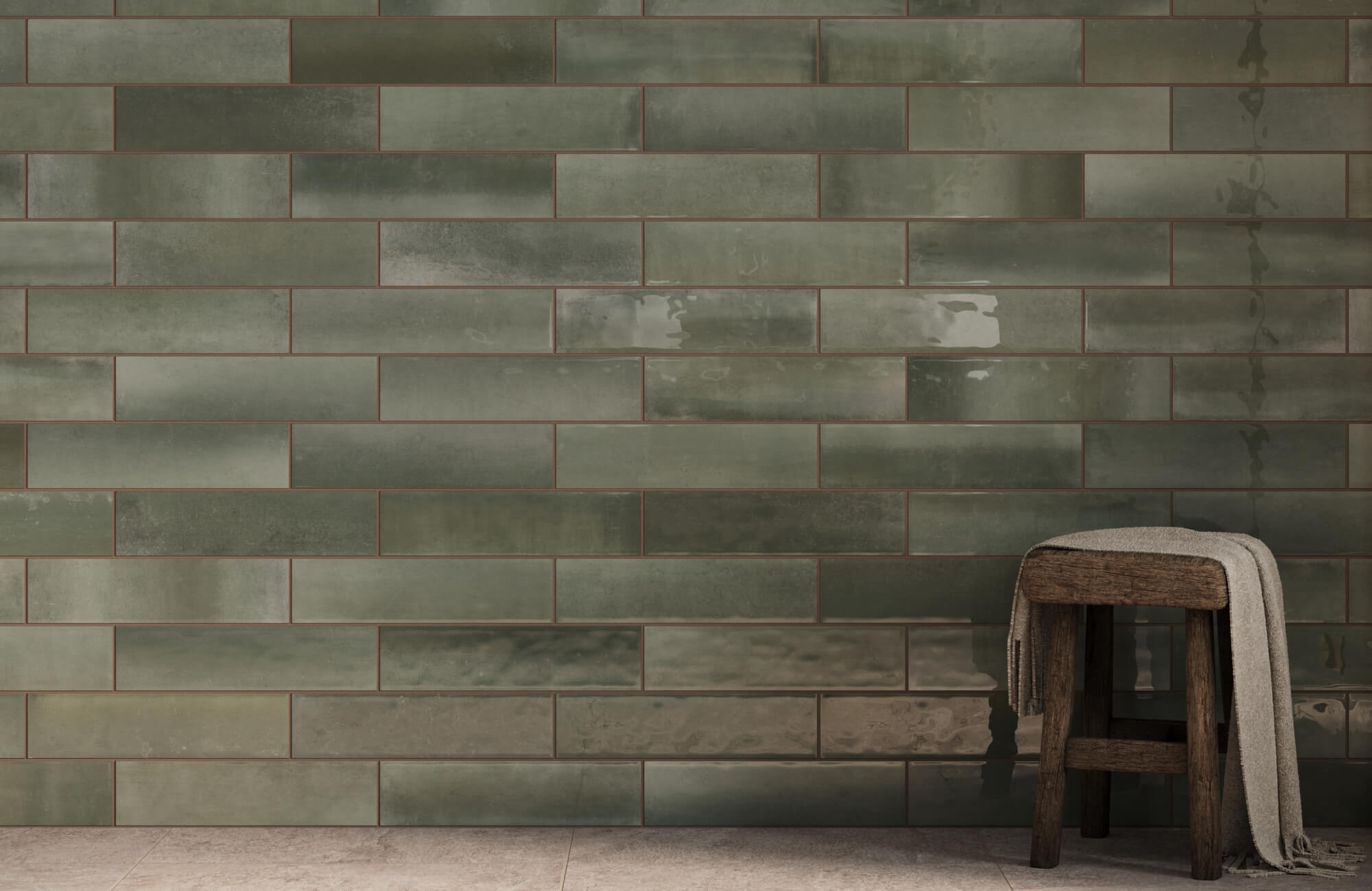 Glossy green subway tiles create a rich, earthy backdrop, paired with a rustic wooden stool draped with a neutral cloth. 