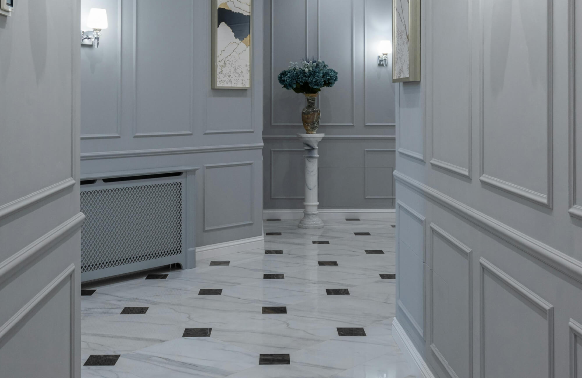 Luxurious white marble floor with contrasting black square accents enhances the elegance of a gray-paneled hallway.