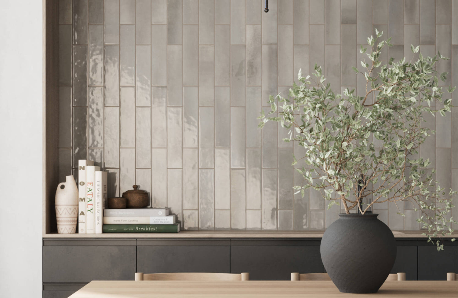 A contemporary accent wall featuring glossy subway tiles in neutral shades, paired with minimal decor and a large matte black vase with greenery.