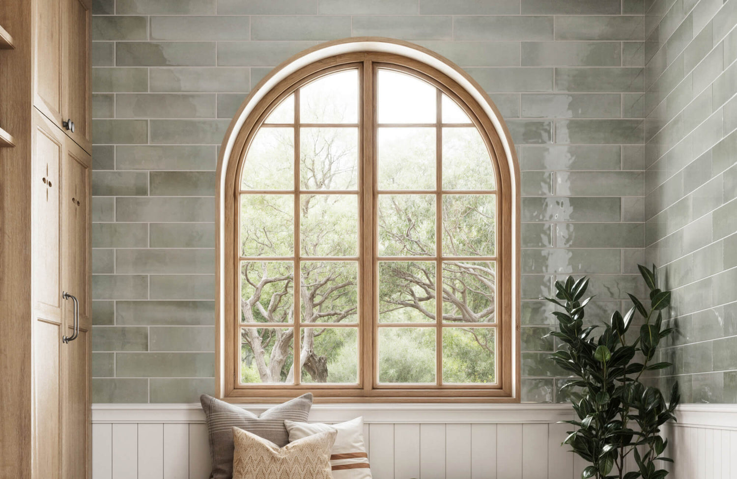 Cozy nook with soft green subway tiles in a staggered pattern and a large arched wooden window, offering a peaceful view of nature.