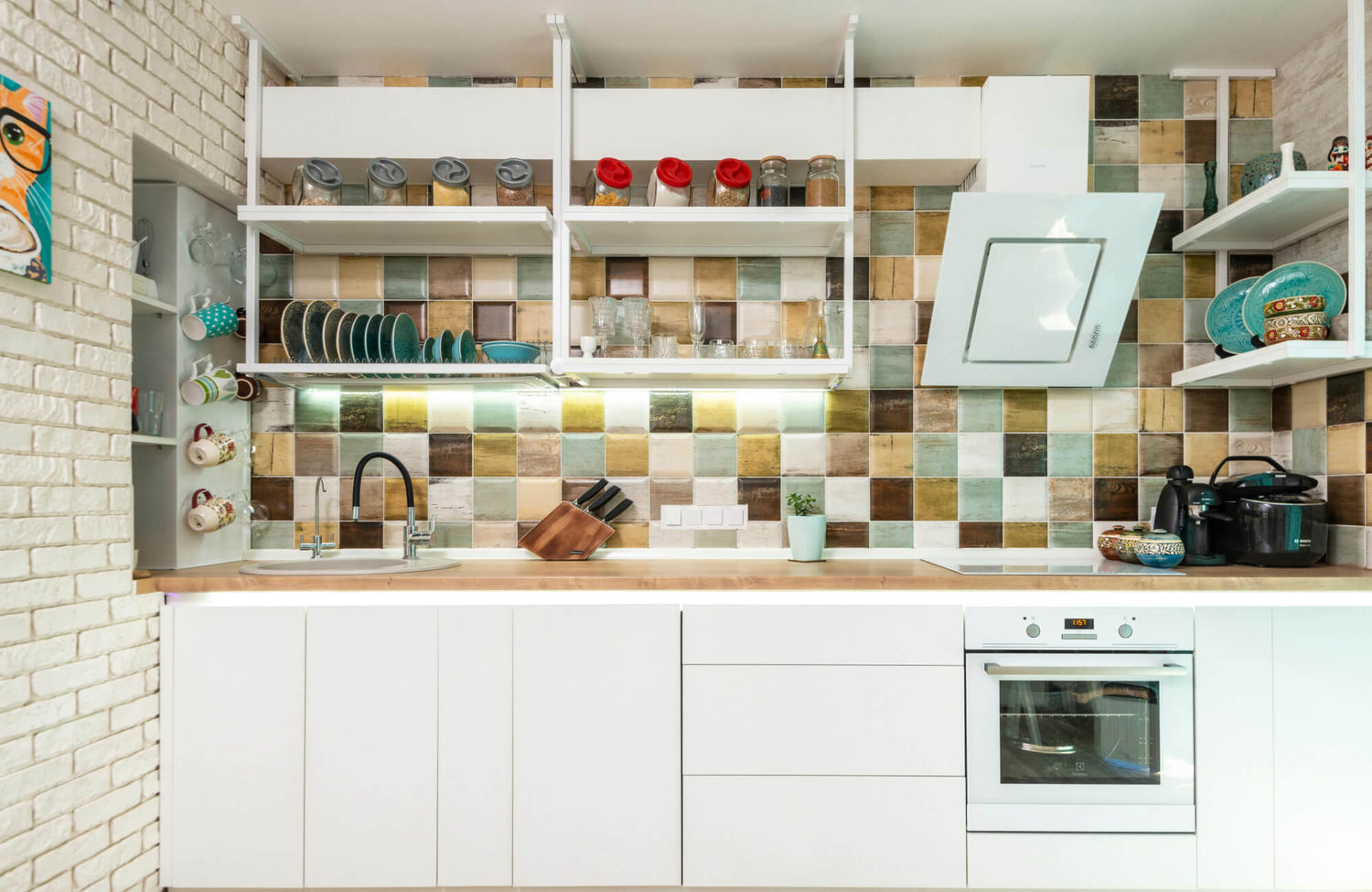 Colorful kitchen backsplash with a mix of green, brown, and beige checkered tiles, complementing white cabinetry and open shelving with modern decor.