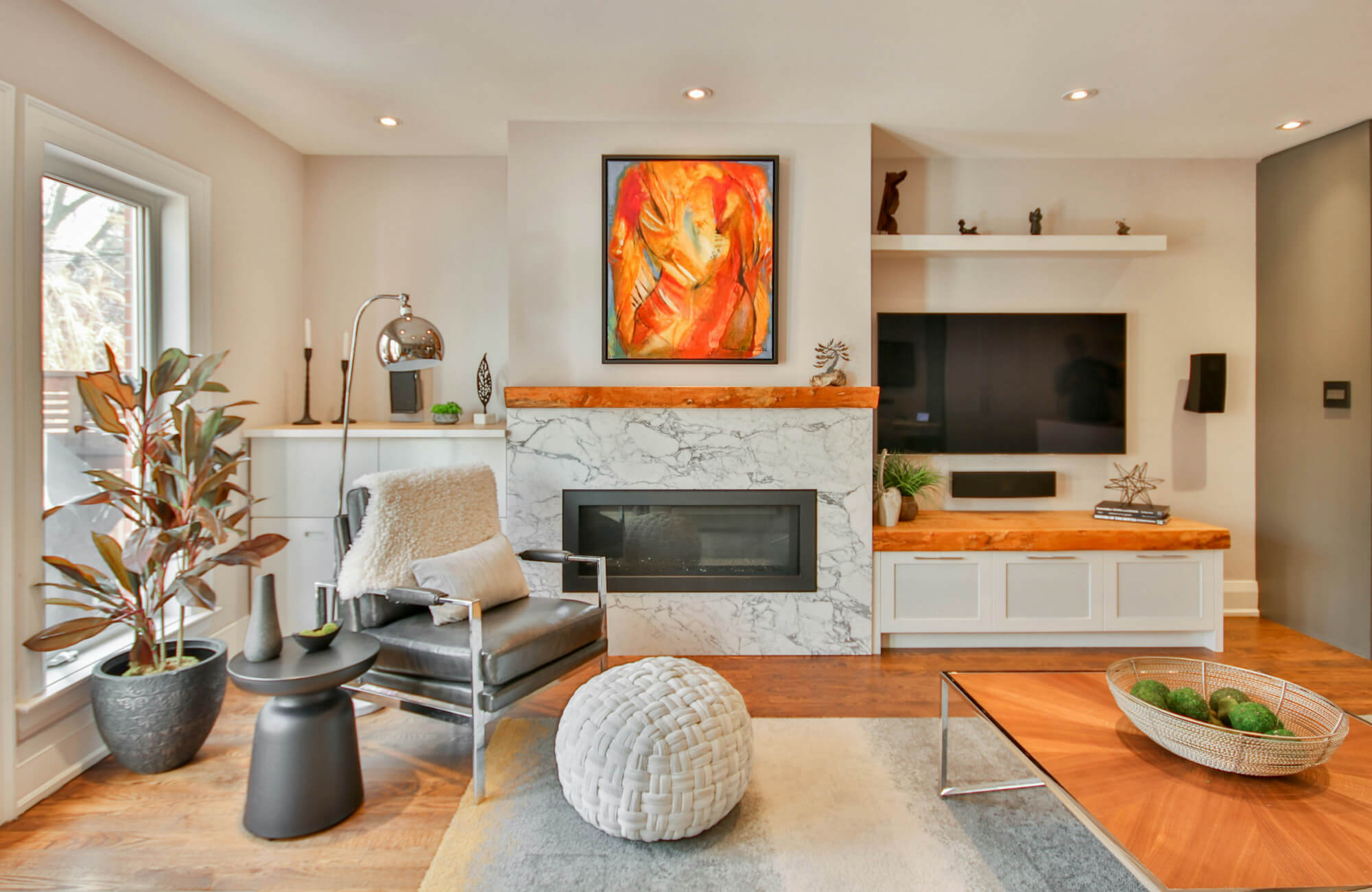 Modern living room with a marble-tiled fireplace, rustic wood mantel, and vibrant abstract artwork, creating a chic and cozy ambiance.