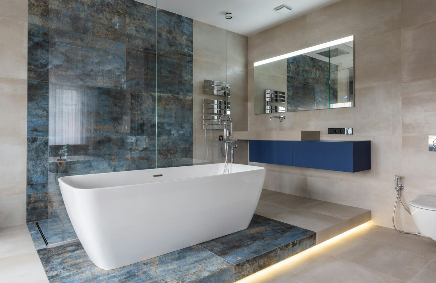 Luxurious modern bathroom with a freestanding tub, featuring bold blue and earthy-toned marble wall and floor accent tiles, a floating vanity, and subtle underlighting for a sleek, spa-like ambiance.