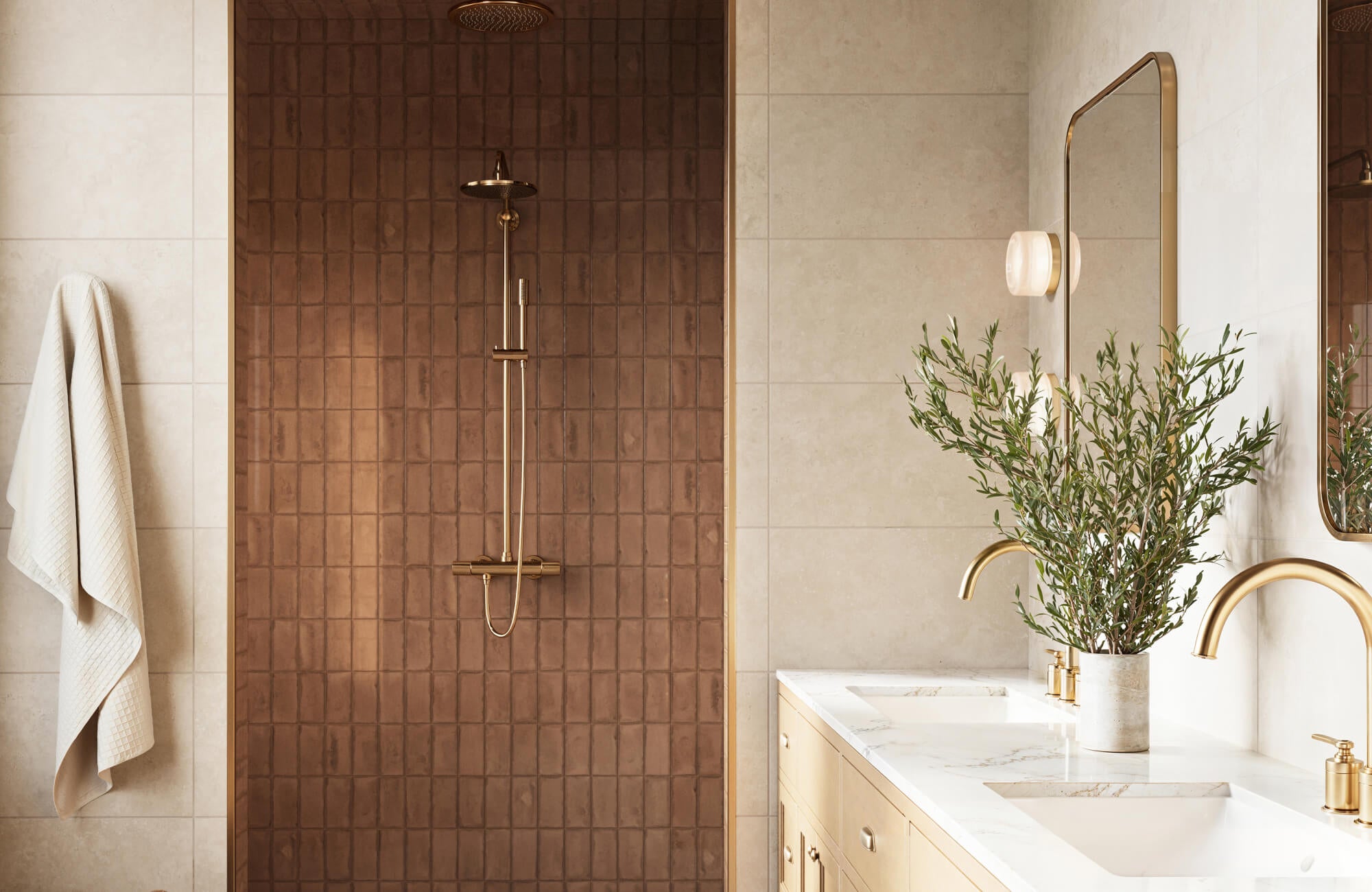 Warm, minimalist bathroom featuring beige wall tiles, a textured subway tile shower with brass fixtures, and a double vanity with gold faucets and a marble countertop.