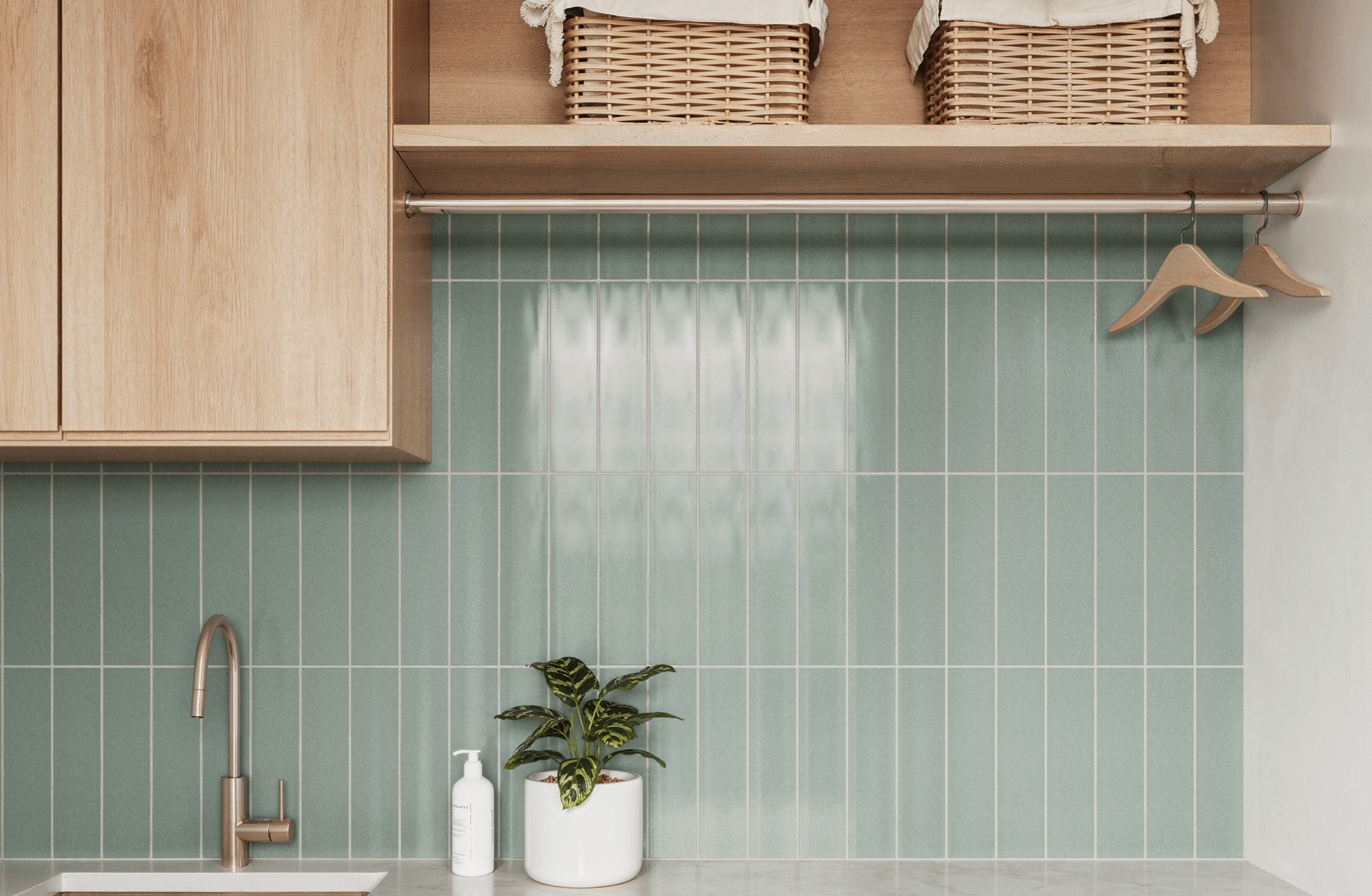 Modern laundry room with vertical light green subway tiles, warm wooden cabinets, and minimalist fixtures, creating a fresh and organized space.