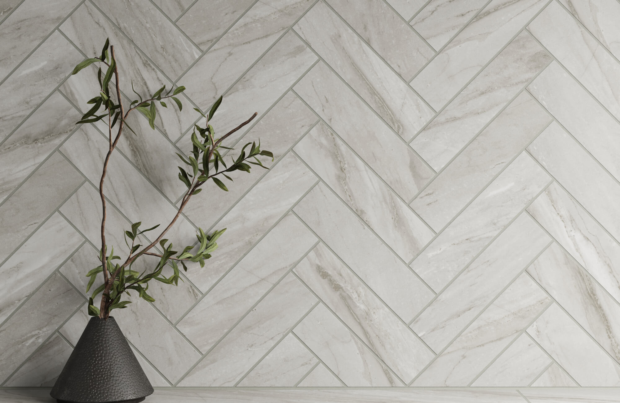 Luxurious kitchen backsplash featuring elegant herringbone subway tile in soft gray tones, paired with a sleek black vase holding an olive branch.