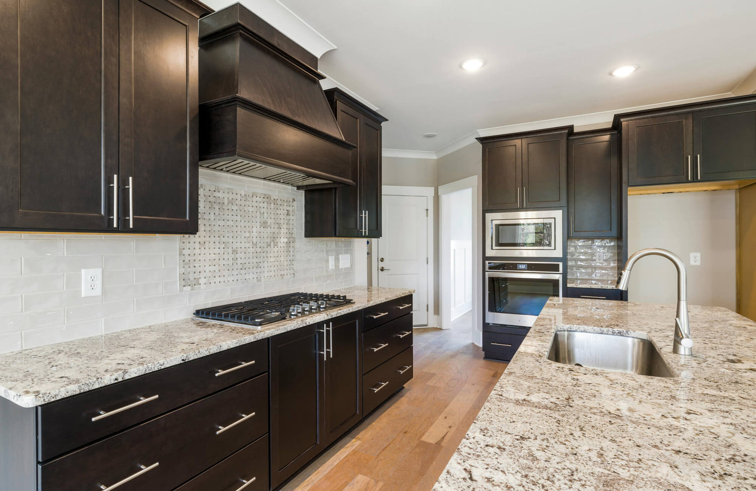 Modern kitchen featuring dark wood cabinets, marble countertops, and a sleek subway tile backsplash.