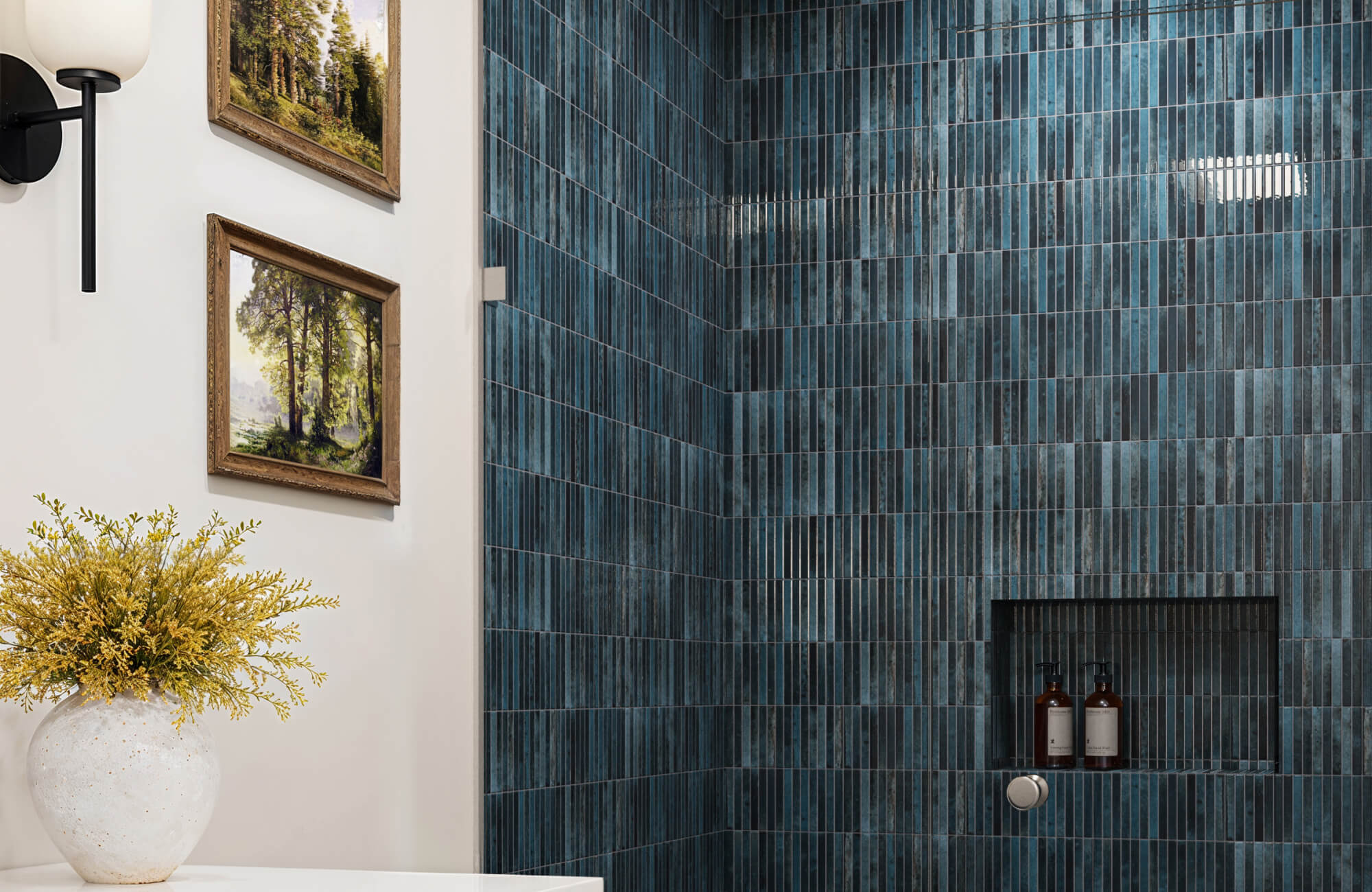 Bathroom showcasing rich blue vertical wall tiles in the shower, adding texture and depth, paired with elegant natural decor and framed art.