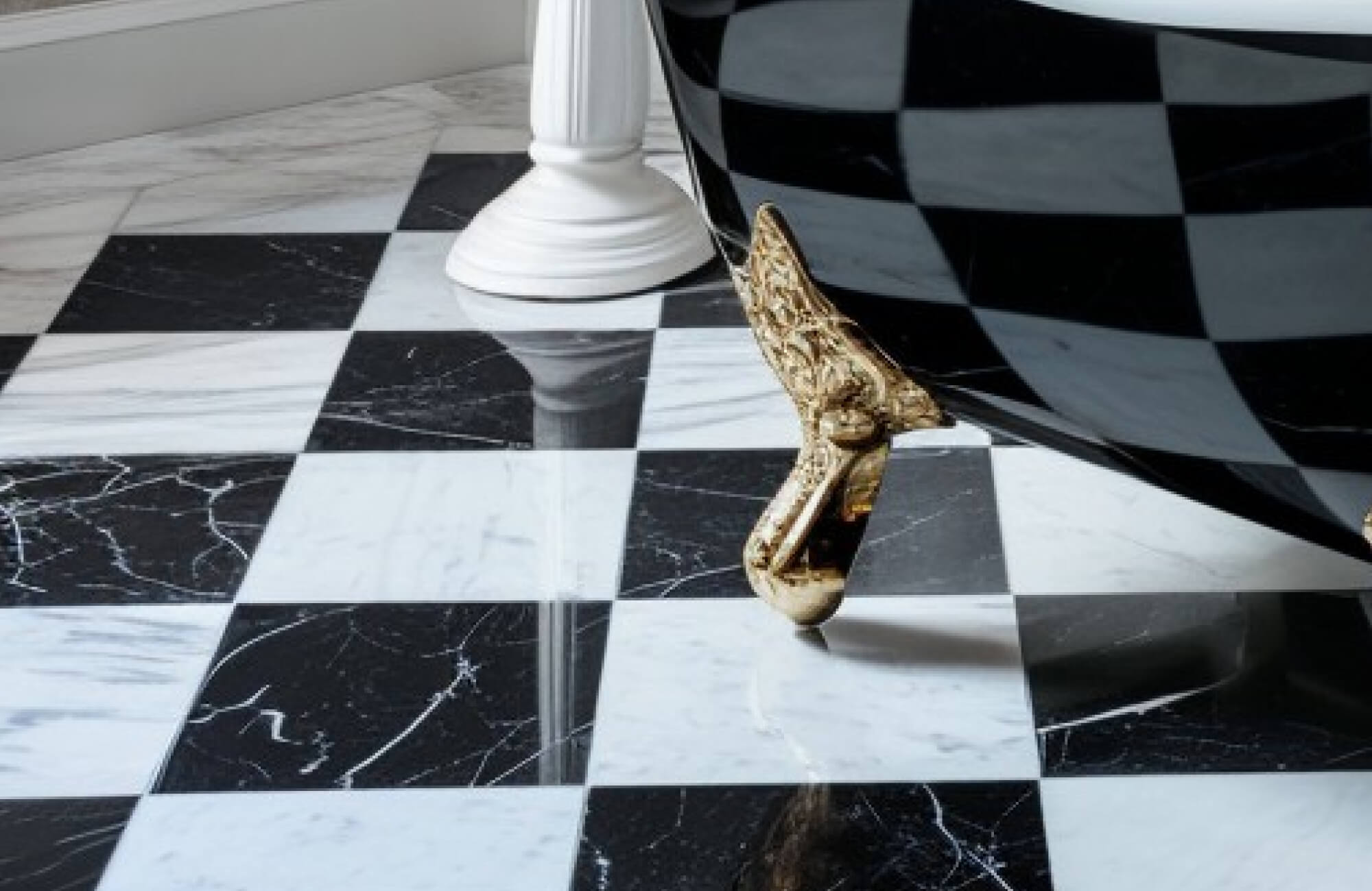 Close-up of a luxurious black-and-white marble checkerboard tile floor, featuring an ornate clawfoot tub. The glossy surface adds a sophisticated elegance to the bathroom setting.