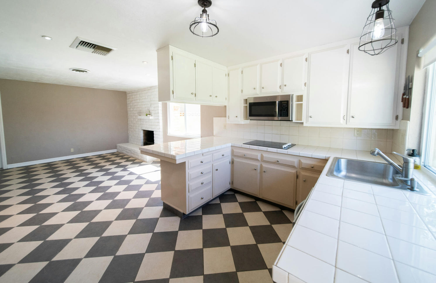 Spacious kitchen with retro black-and-white checkerboard flooring, white cabinetry, and a bright, open layout with a cozy fireplace.