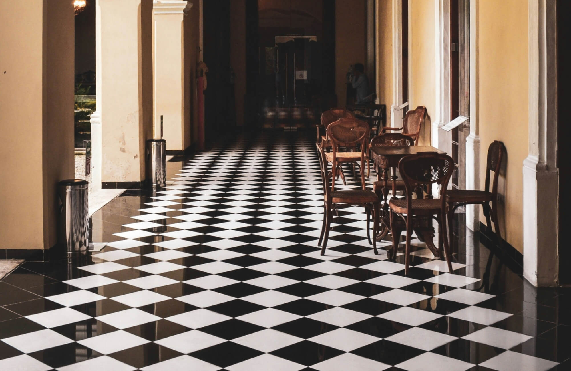 Elegant corridor with black and white checkerboard floor tiles, wooden chairs, and tables against yellow walls