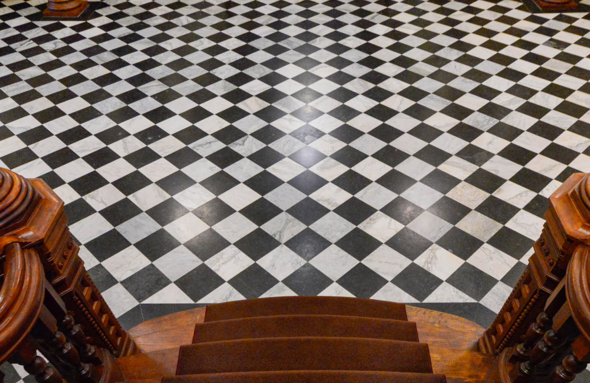 Grand foyer with classic black and white checkered marble floor, viewed from a descending wooden staircase.