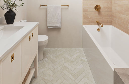 Stylish bathroom with herringbone floor tiles, gold fixtures, and a warm beige brick accent wall for a modern, elegant look.