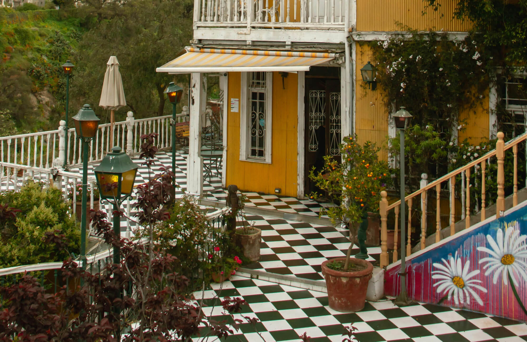 Charming outdoor patio with a black and white checkerboard tile floor, vibrant yellow walls, and lush greenery, creating a cozy and inviting ambiance.