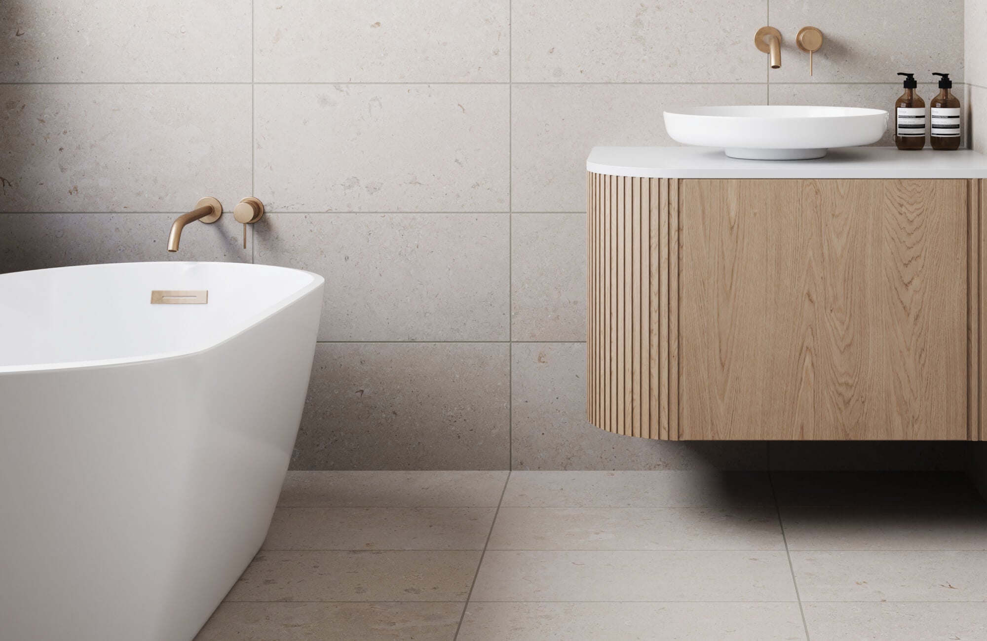 Minimalist bathroom featuring large stone tiles, a freestanding white tub, and a wooden vanity with brass fixtures.