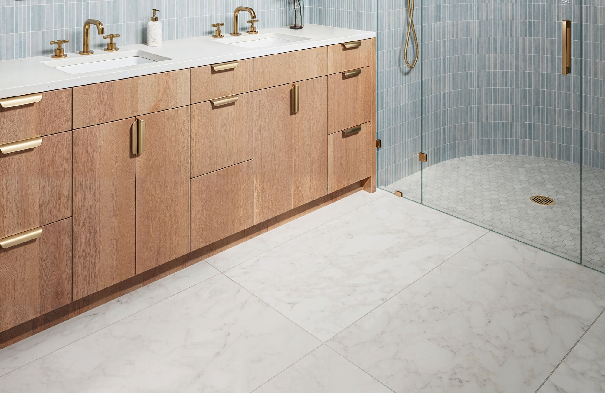 Light marble floor tiles bring an airy elegance to this bathroom, paired with a wood vanity and brass fixtures for a warm, modern aesthetic. 