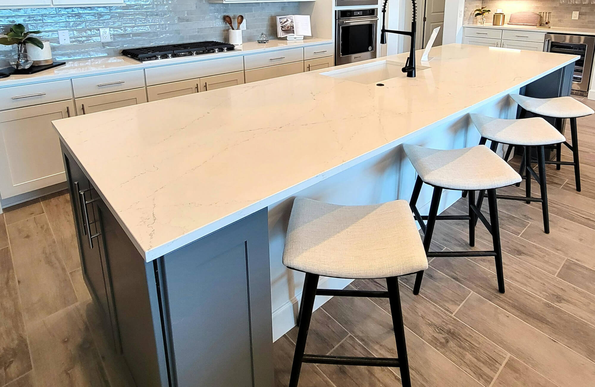 Modern kitchen with a large white island countertop, beige cabinetry, and wood-look tile flooring.