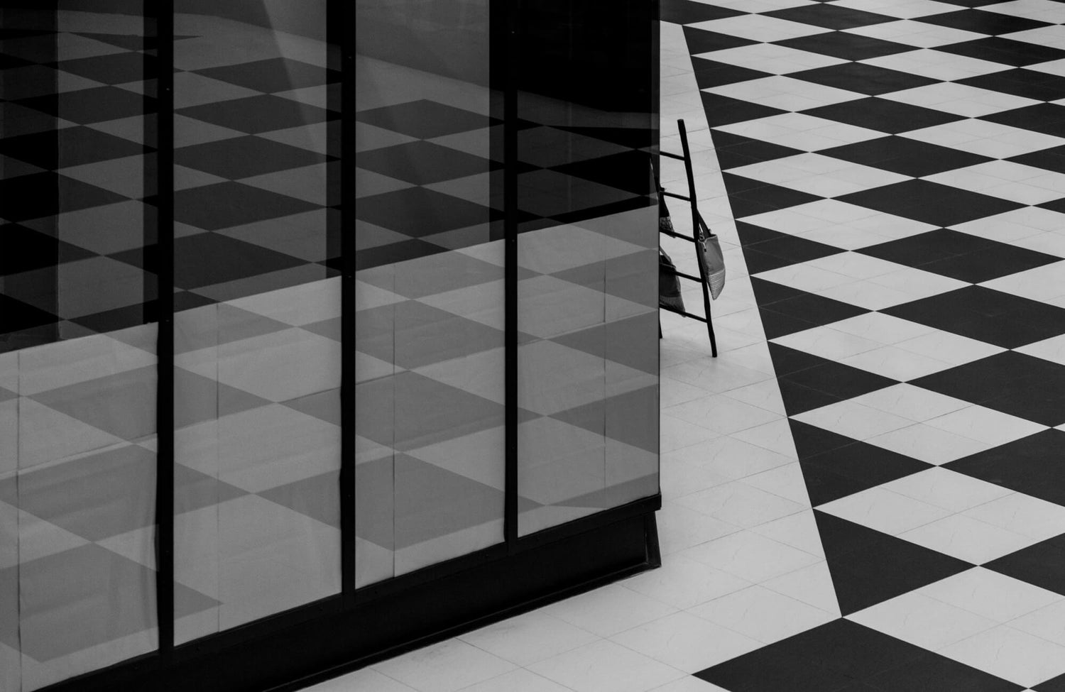 Modern interior with black and white checkerboard tiles, reflective glass walls, and a ladder with hanging bags, creating a sleek and geometric aesthetic