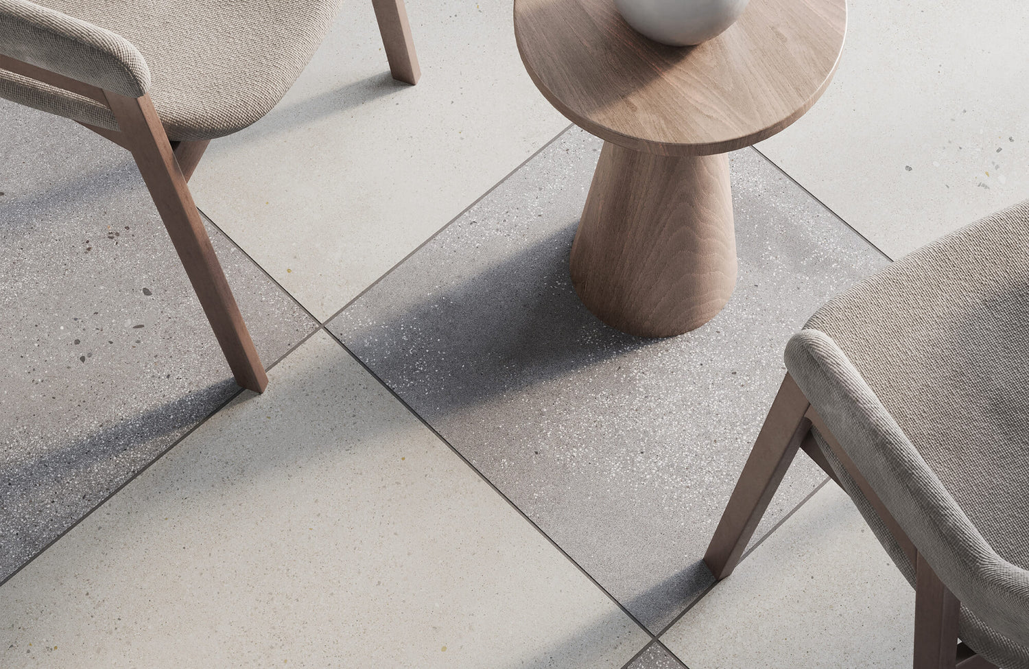 Top view of a modern space with large gray and white checkered tiles with speckles, a wooden side table, and fabric-covered chairs