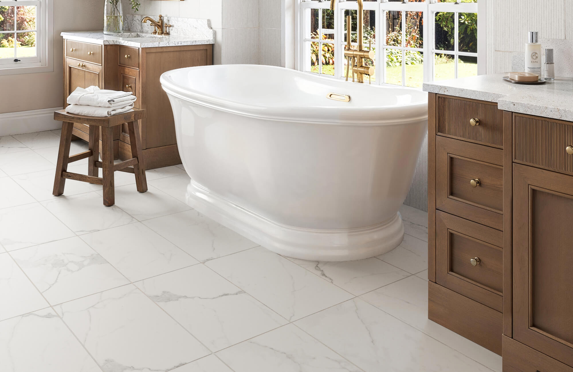 Luxurious bathroom with a freestanding white bathtub, marble-look floor tiles, and warm wooden cabinetry, creating an inviting and serene atmosphere.