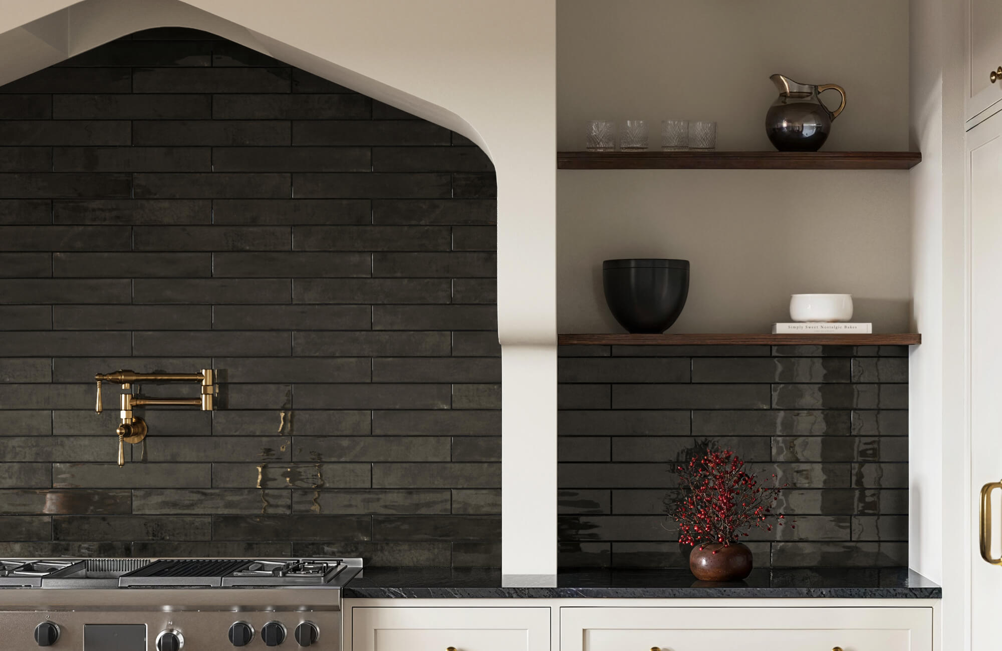 Elegant kitchen with sleek black subway tiles, brass faucet fixtures, and minimalist wooden shelves displaying modern decor.