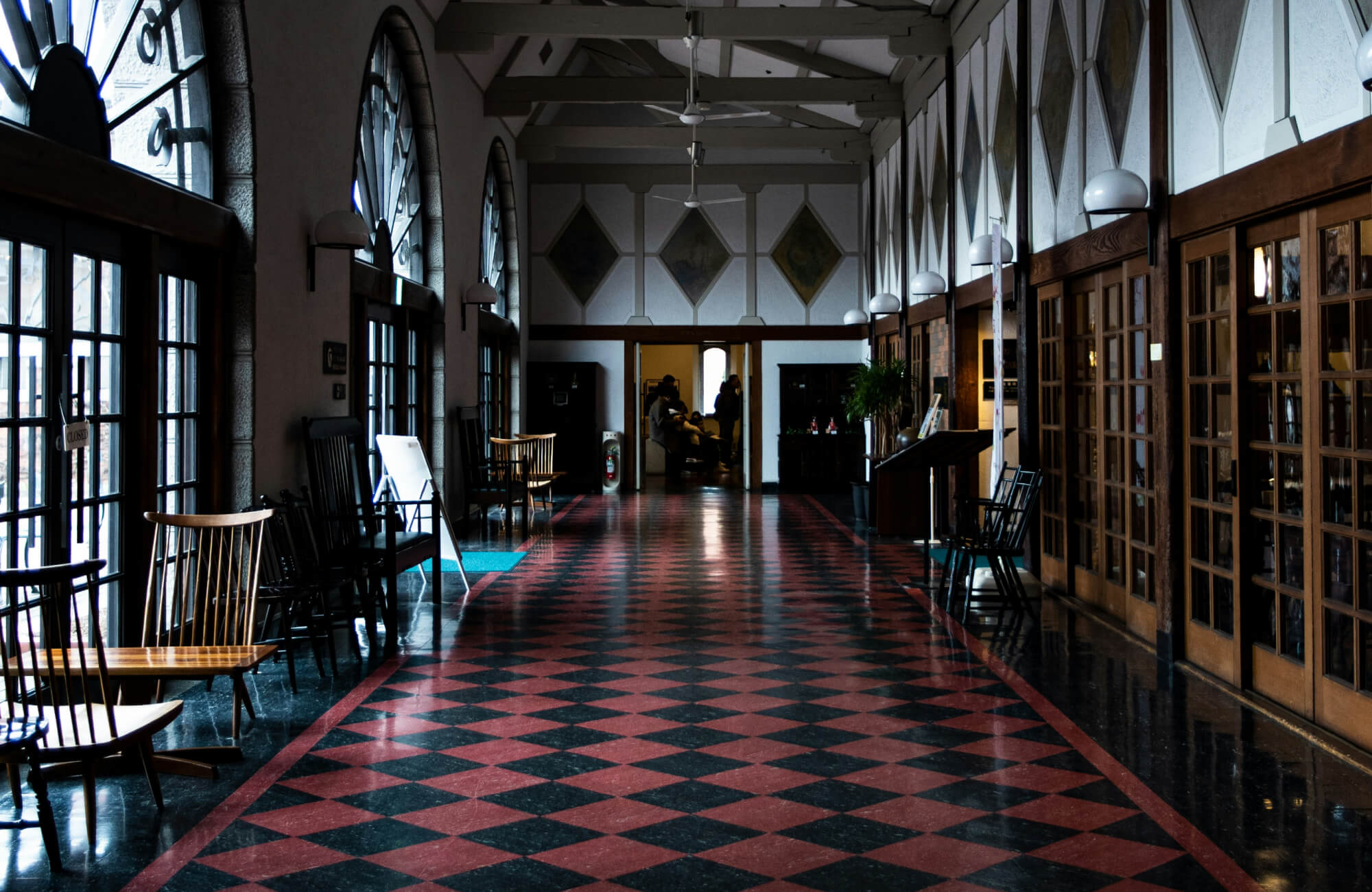 A majestic hallway with arched windows and a striking red and black checkered tile floor, creating a dramatic and elegant atmosphere.