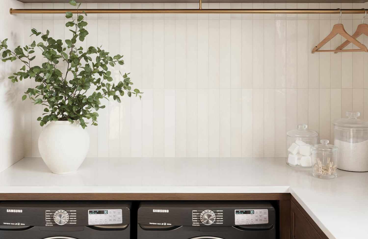 Glossy white vertical subway tiles create a sleek and clean backdrop in a modern laundry room, accented by a gold rod and natural decor.