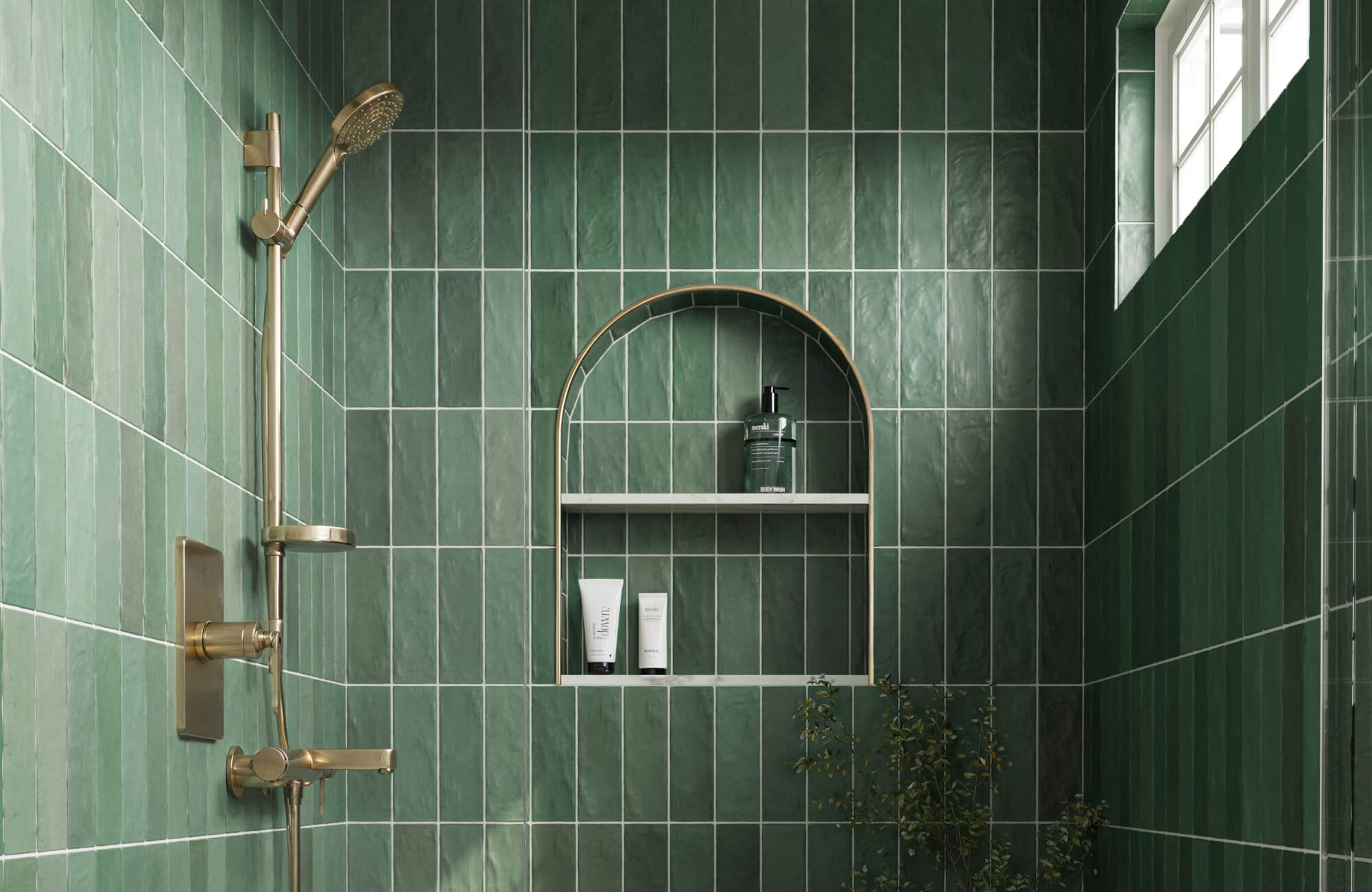 Luxurious shower featuring matte green subway tiles, accented by elegant gold fixtures and a built-in arched shelf, creating a serene and sophisticated space.