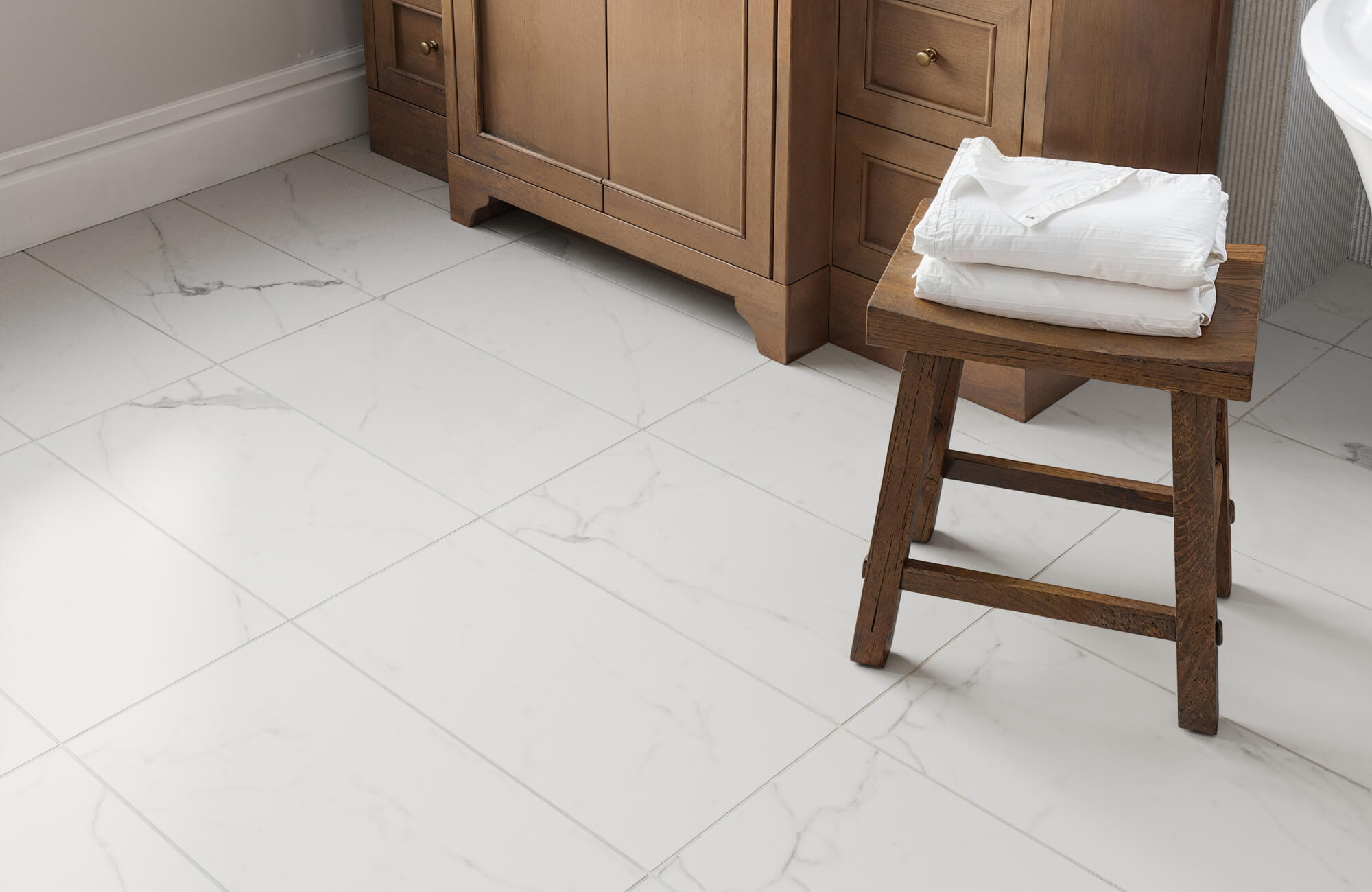 Large white marble look tiles with subtle gray veining as flooring, complementing warm wooden cabinetry in a bathroom.