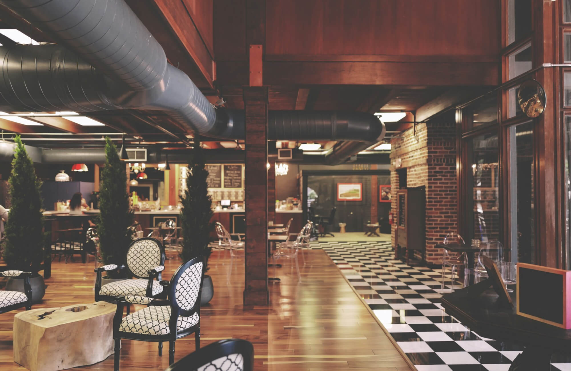 A cozy cafe featuring a mix of wooden flooring and a classic black and white checkerboard tile pattern, with stylish seating and a warm, inviting ambiance