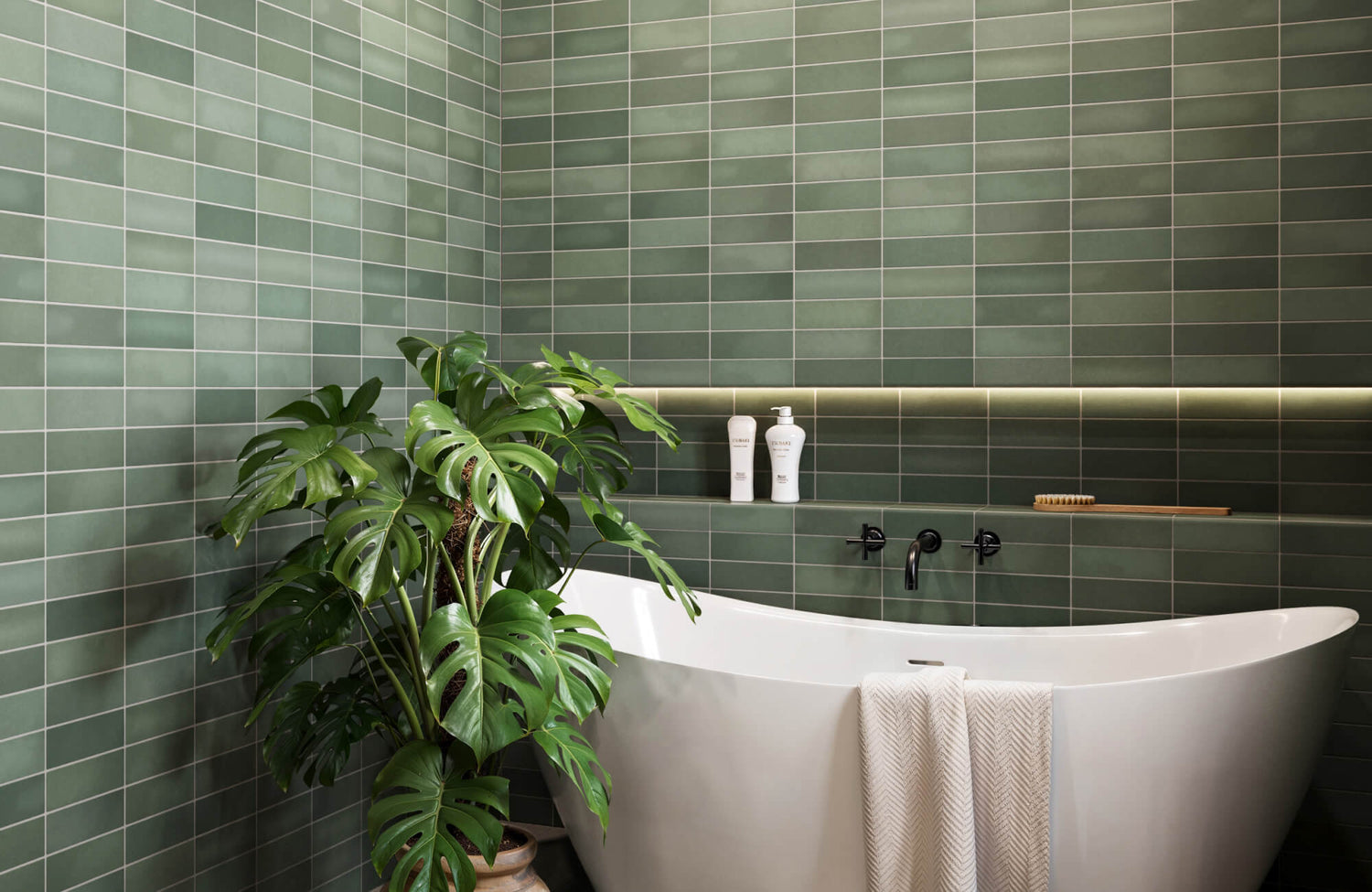 Modern bathroom with rich moss green subway tile walls, a sleek white freestanding tub, and lush monstera plant decor.