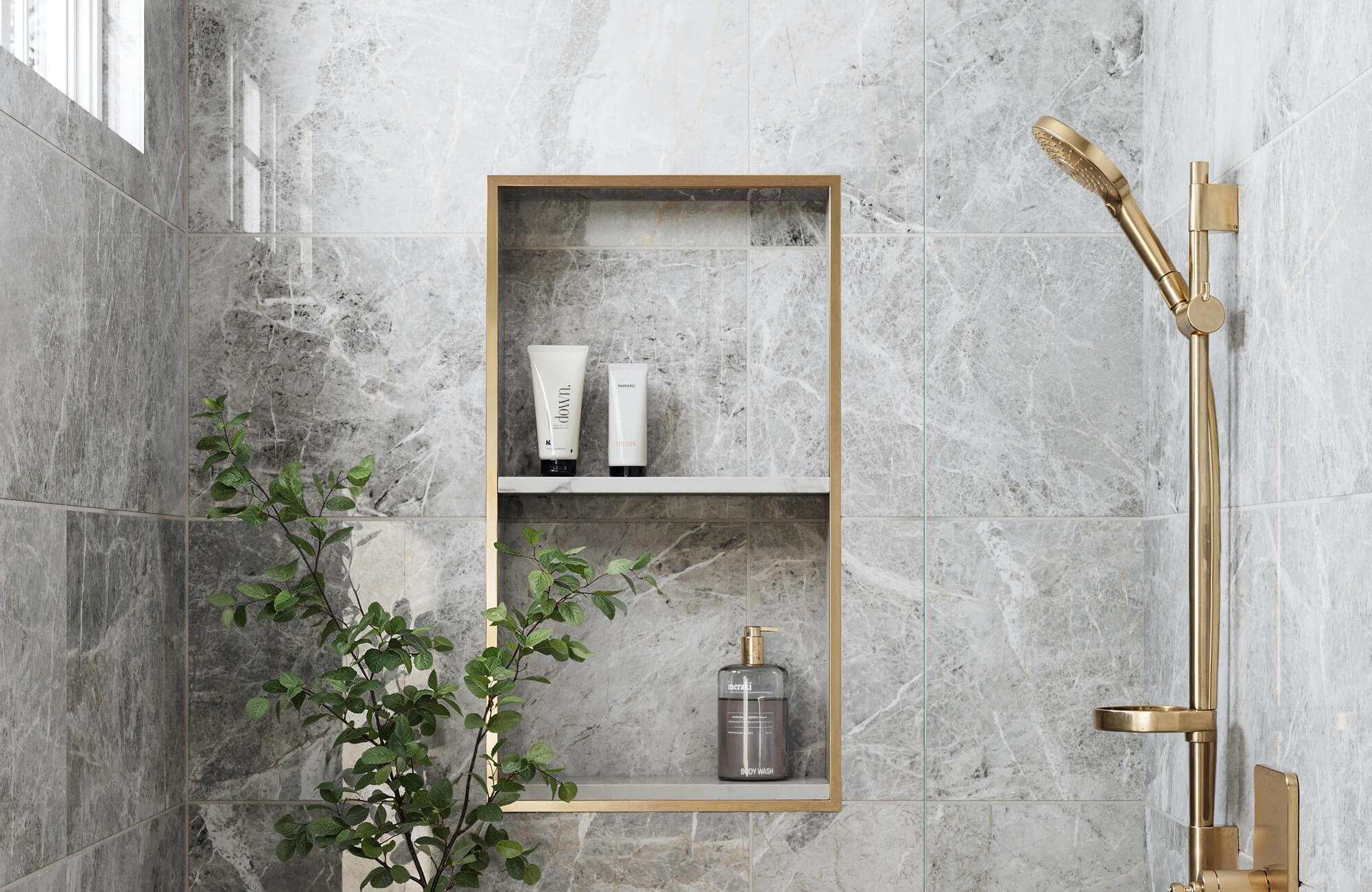 Luxurious grey marble-look tiles line a modern shower with a golden shower head and shelving, adding elegance and a refined touch to the space.