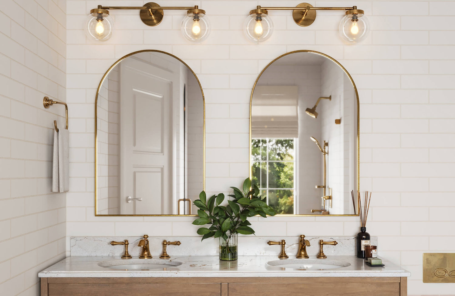 Elegant bathroom with white subway tiles, dual sinks with brass fixtures, and arched mirrors for a chic, modern aesthetic.