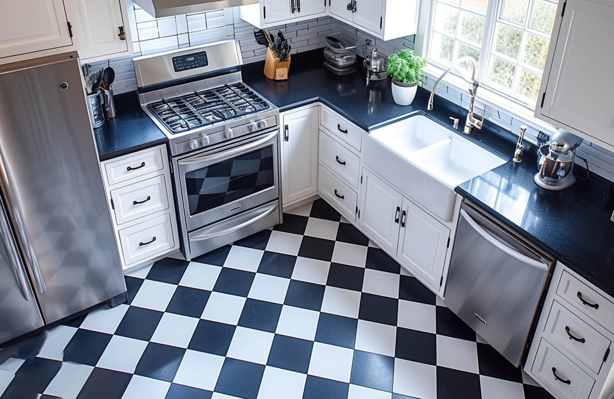 Bright kitchen featuring classic black-and-white checkerboard flooring, sleek white cabinetry, stainless steel appliances, and dark countertops.