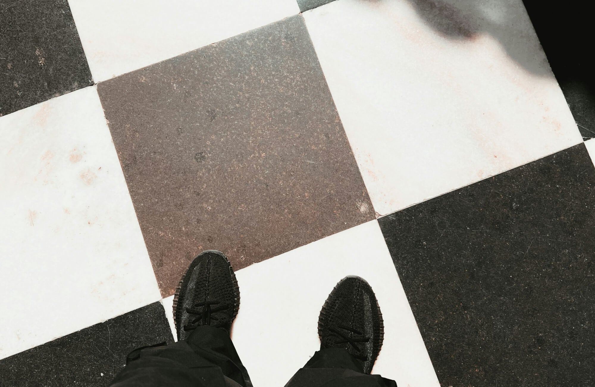 Close-up of feet in black sneakers standing on a black and white checkerboard tile floor, highlighting the classic contrasting pattern
