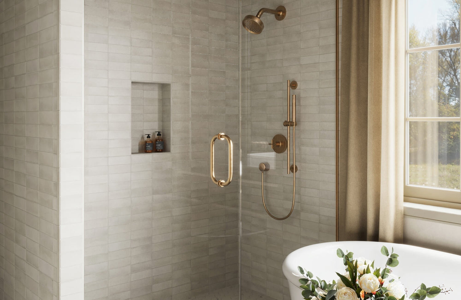 Bright bathroom featuring oat subway tiles, a frameless glass shower, gold fixtures, and a freestanding tub accented with fresh floral decor.