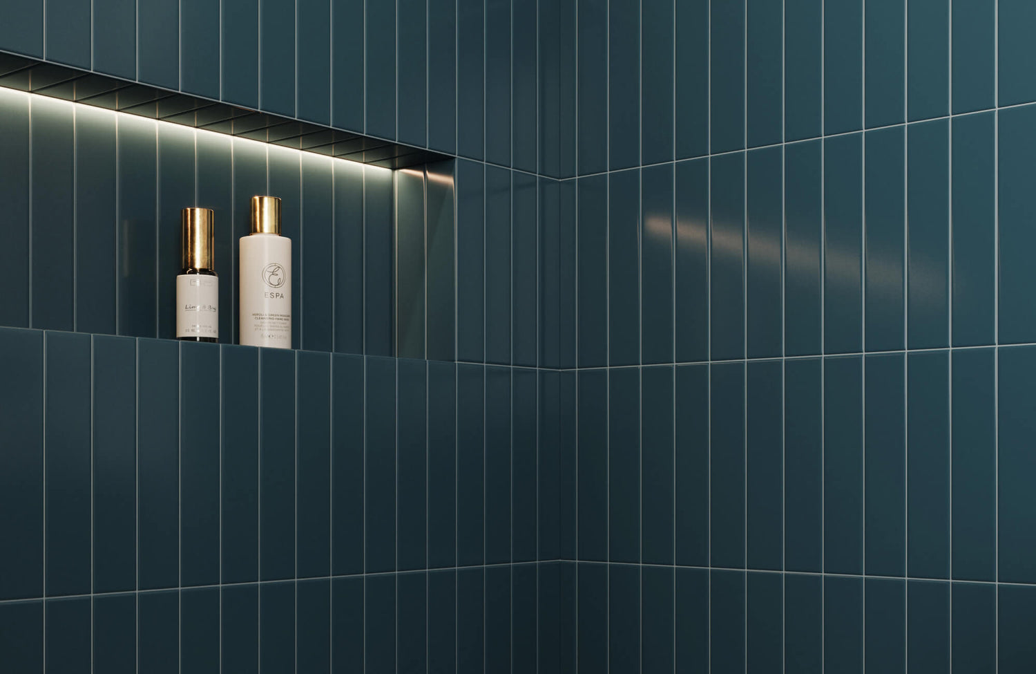 Glossy teal subway tiles with clean, vertical lines frame a recessed niche illuminated by subtle LED lighting, showcasing golden-capped toiletries. 