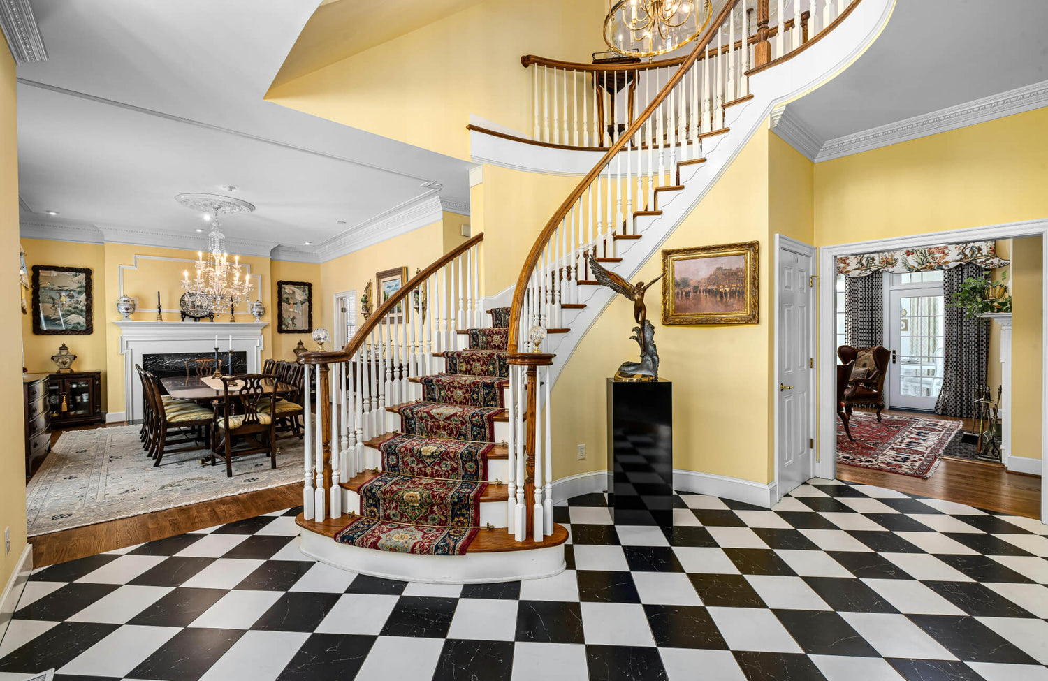 Grand entryway featuring a curved staircase with patterned carpet, yellow walls, and a black-and-white checkered tile floor.