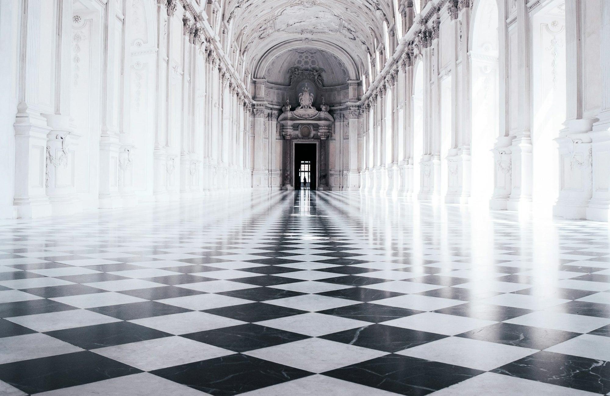 Majestic hallway with high vaulted ceilings, adorned with black and white checkered marble floors, leading to a grand doorway