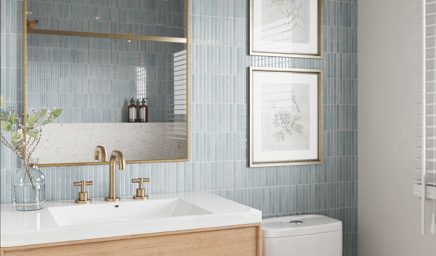 Soft blue vertical tiles add a serene touch to this bathroom, complemented by brass fixtures and framed botanical prints, creating a tranquil and elegant space