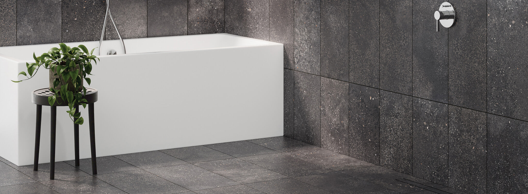 Modern bathroom with dark terrazzo-look tiles, featuring a sleek white bathtub and a stylish plant on a black stool