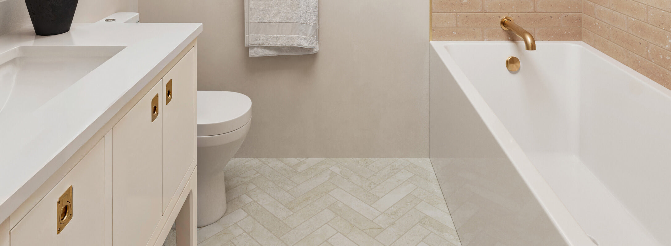 Elegant bathroom featuring beige subway tile flooring in a herringbone pattern, a white bathtub, and gold fixtures, complemented by a sleek vanity