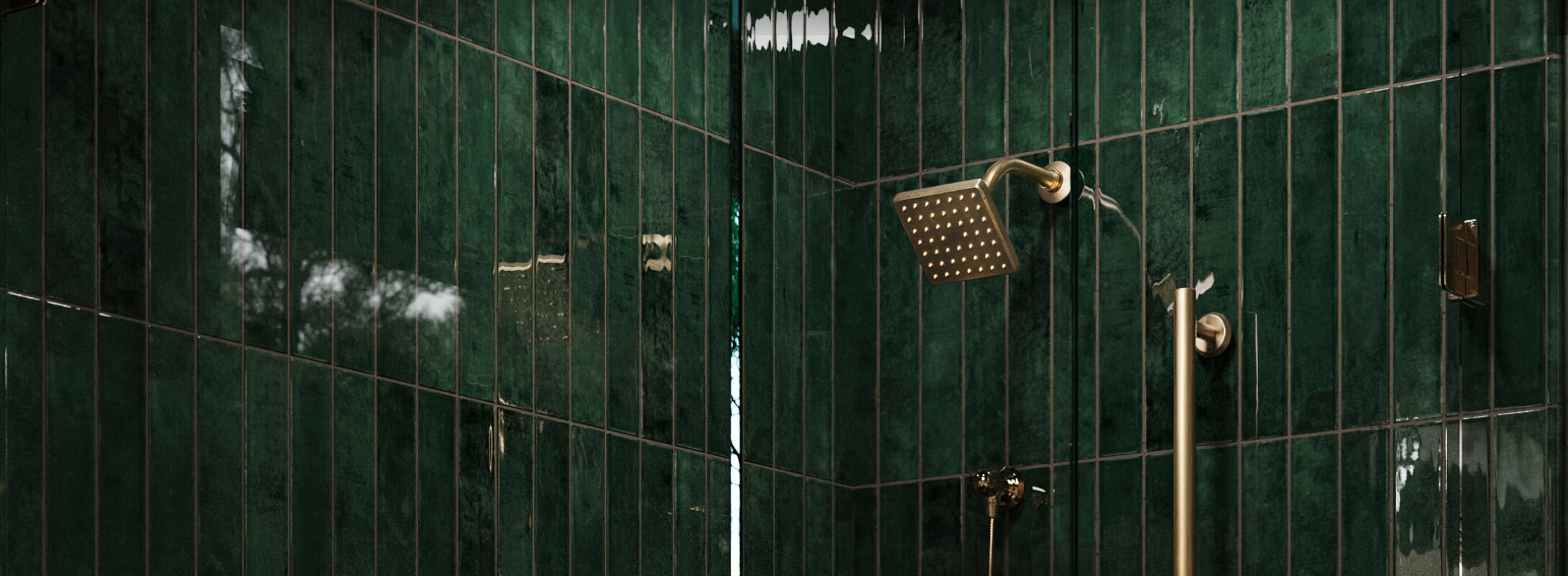 Luxurious bathroom with glossy green subway tiles and a sleek brass showerhead, creating an elegant and modern look