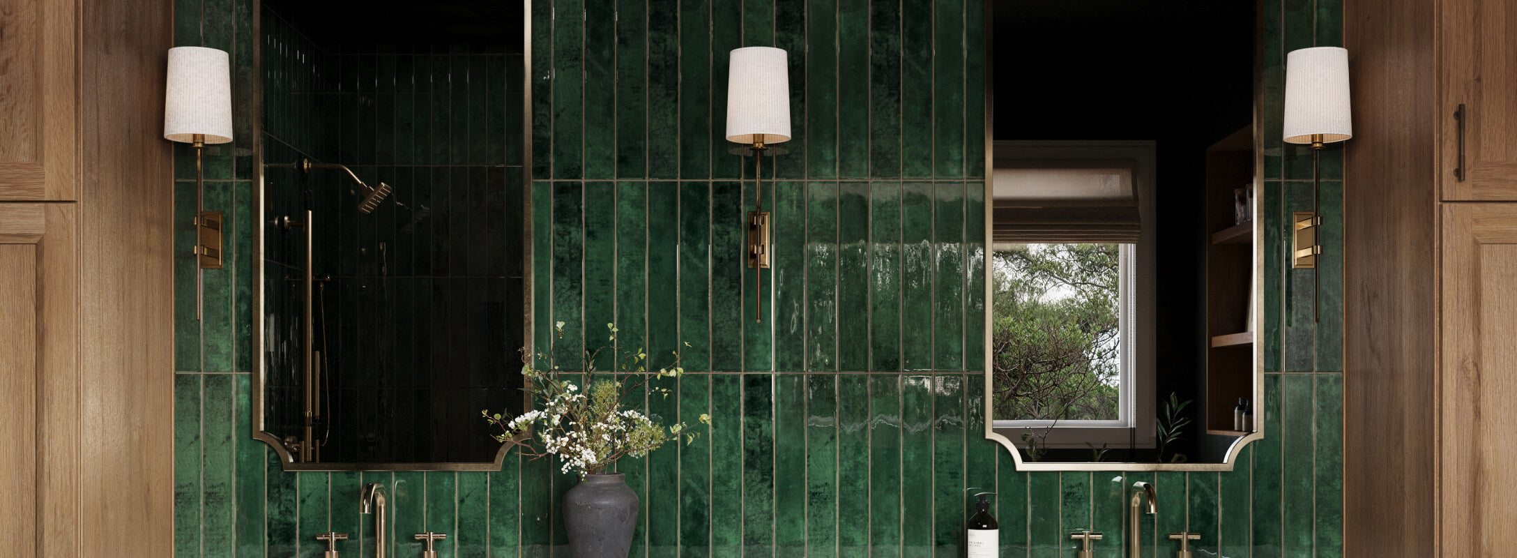 Rustic bathroom featuring glossy emerald green tiles, brass fixtures, and natural wood cabinetry, accented by elegant lighting and fresh florals