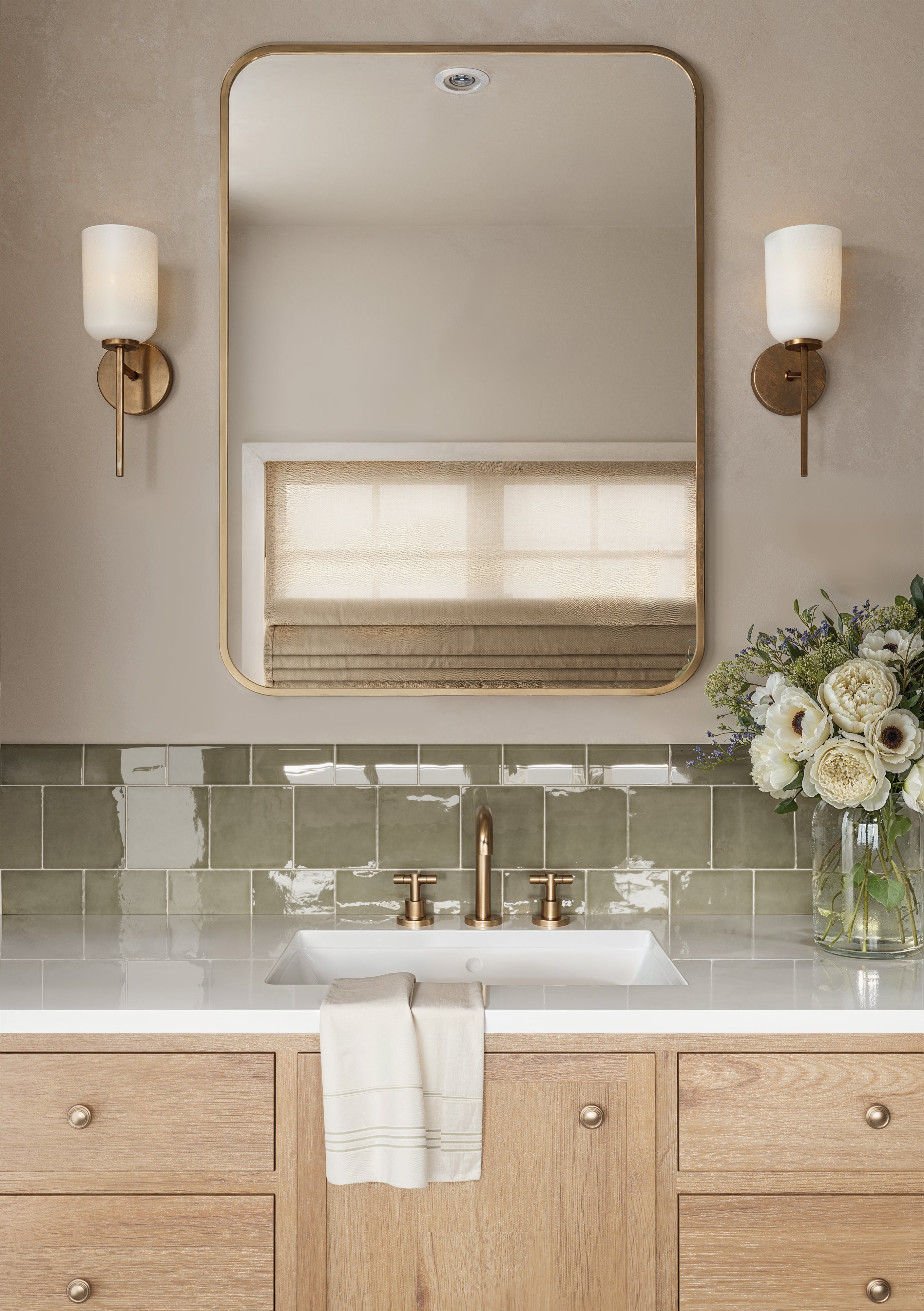 Elegant bathroom vanity with glossy olive green Mikayla bullnose tiles, warm wood cabinetry, and gold fixtures beneath a modern framed mirror