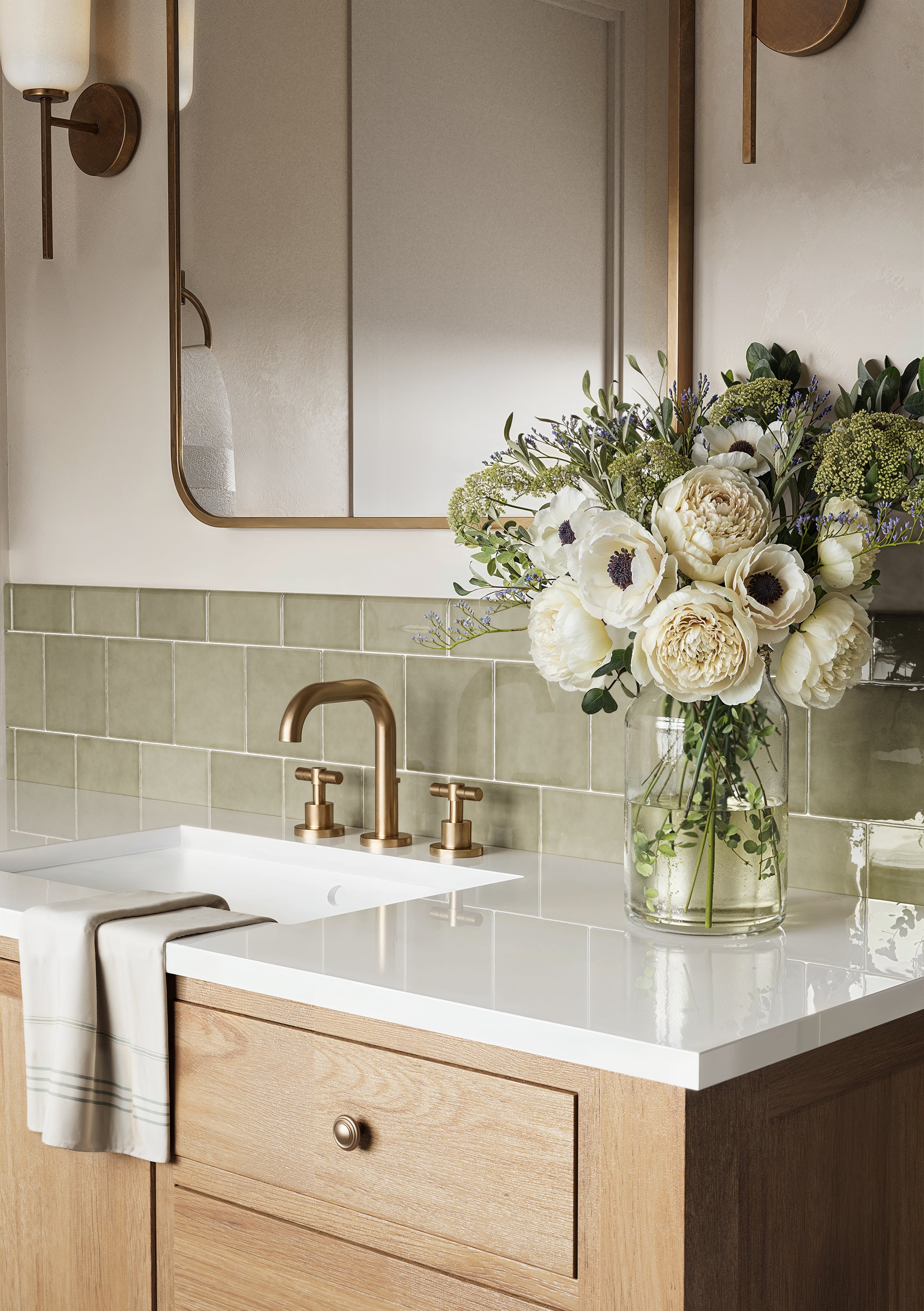 Close-up of a bathroom vanity showcasing glossy Mikayla olive green bullnose tiles, gold fixtures, and a vase of white flowers on a sleek countertop